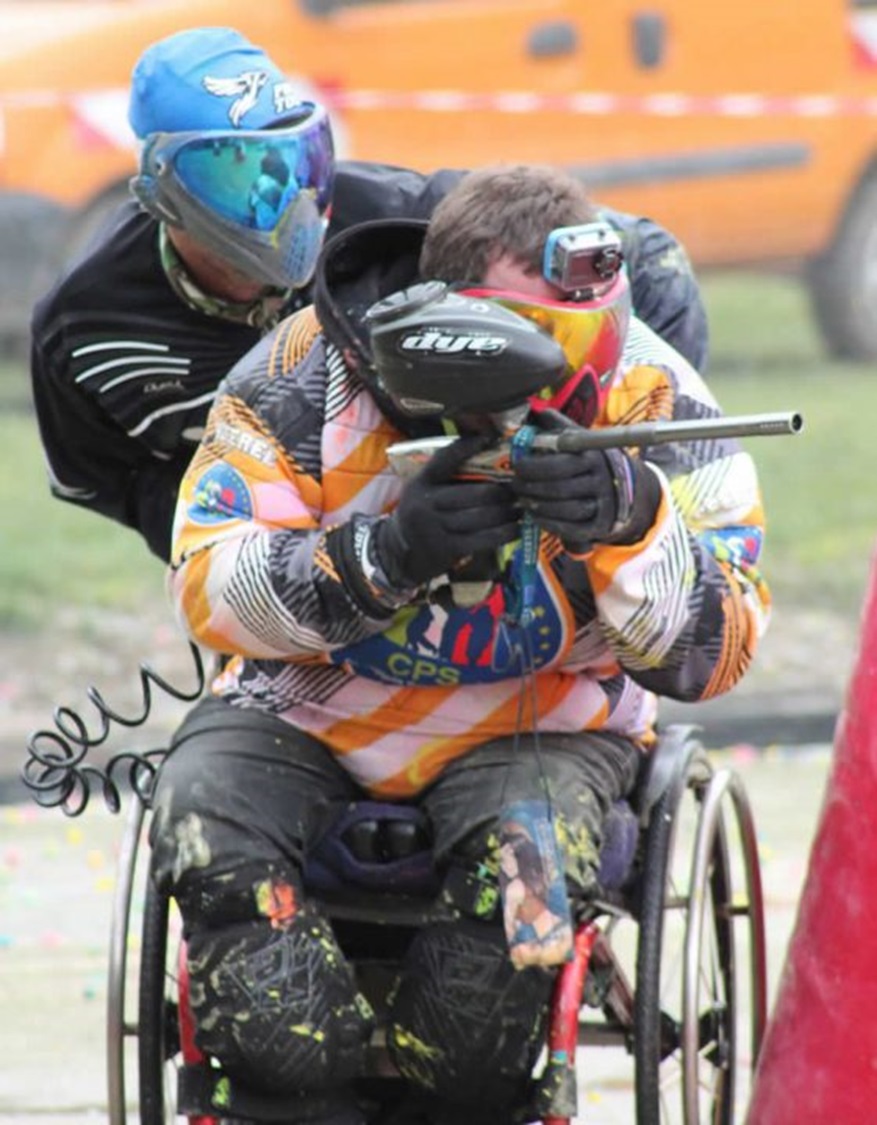 Un joueur en fauteuil roulant concentré et déterminé pendant une session de paintball, montrant que le handicap n'est pas un obstacle à la participation.